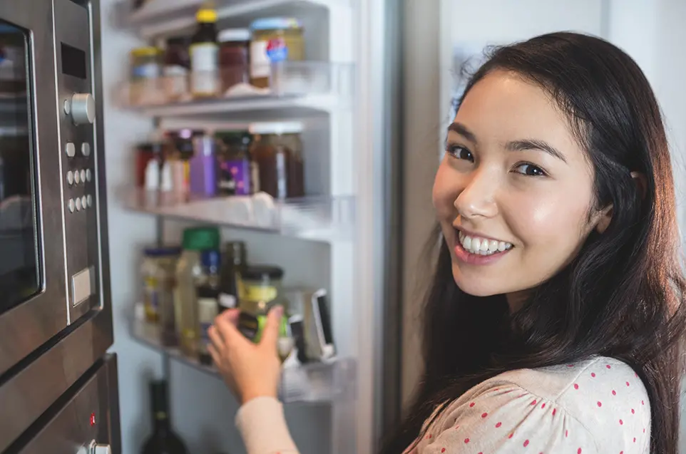 kvinna tittar i kameran, står vid öppet kylskåp