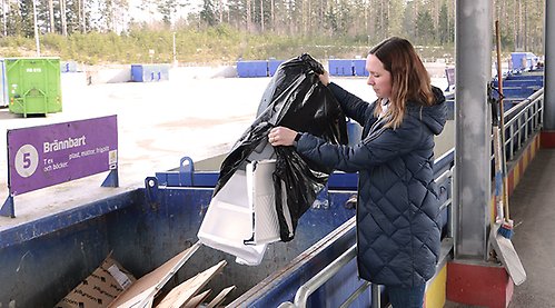 Kvinna tömmer ut säck i container på återvinningscentral